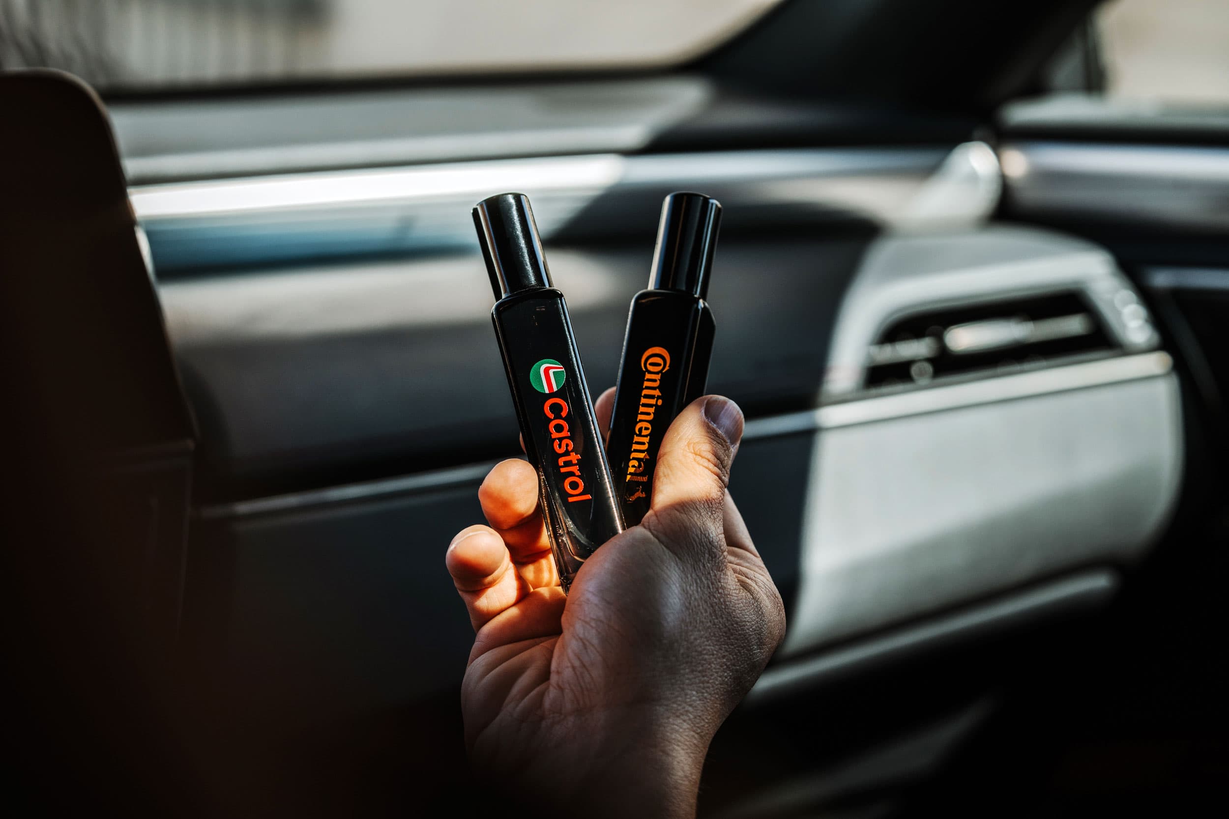Două flacoane spray personalizate, ținute într-un interior auto.